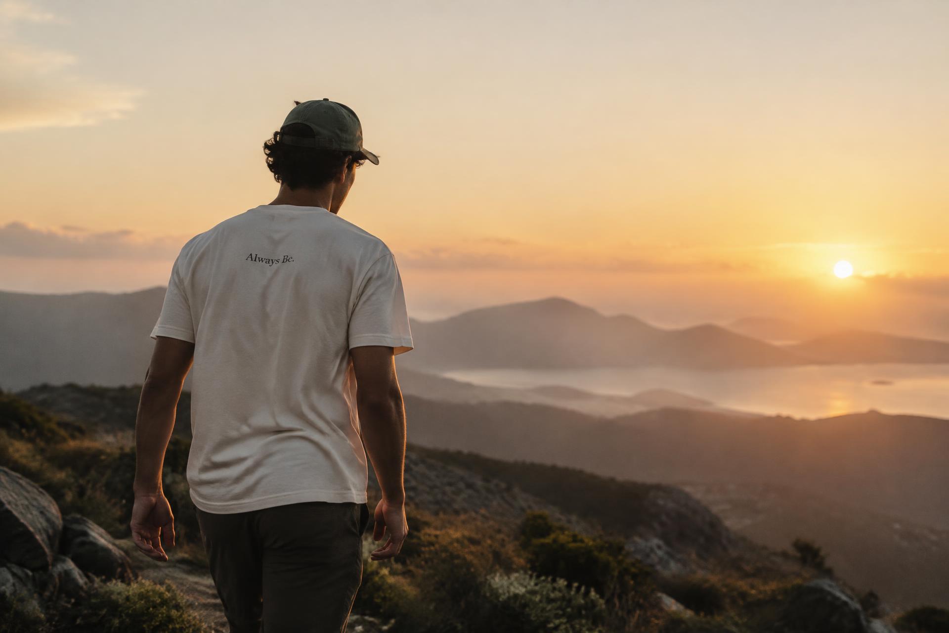 A young adult in an Always Be shirt walking toward a mountain sunrise